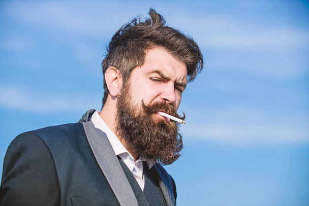 Truth about smoking pleasure and nicotine addiction. Bearded hipster smoking cigarette blue sky background. Guy with cigarette enjoy nicotine influence. Man with beard and mustache hold cigarette - Foto, Bild