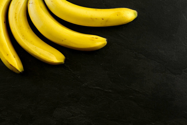 Tabletop view - four bananas on black stone like board, space fo - Фото, изображение