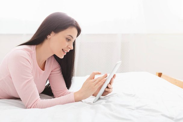 Menina alegre navegando no tablet digital, descansando na cama
 - Foto, Imagem