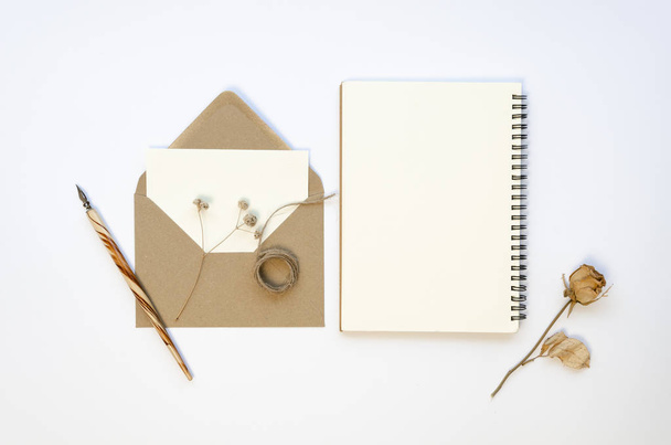 Flat lay mockup aperto notebook a spirale vuota e busta di carta marrone con forbici, spago e penna inchiostro su un tavolo bianco. Rosa secca su sfondo bianco
 - Foto, immagini
