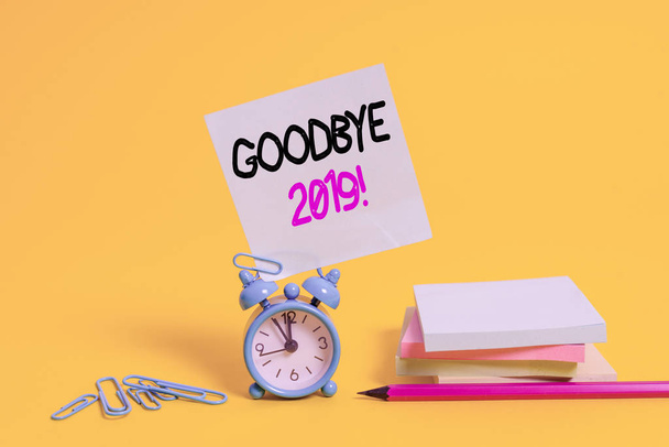 Conceptual hand writing showing Goodbye 2019. Concept meaning express good wishes when parting or at the end of last year Alarm clock pencil clips note stacked notepads colored background - Photo, Image