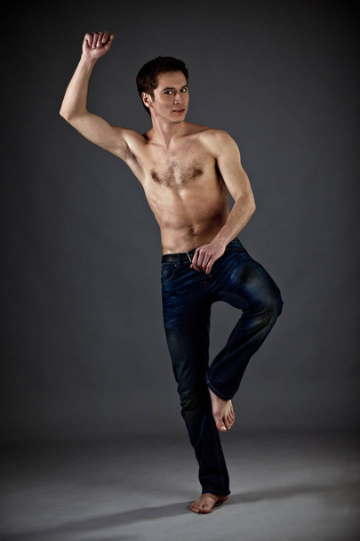 Young athletic man with naked torso in jeans standing over black background - Φωτογραφία, εικόνα