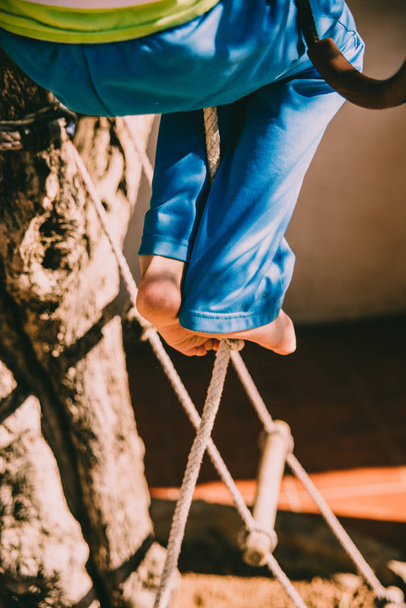 Bare feet of a boy holding on to a rope while climbing up it. - Photo, Image