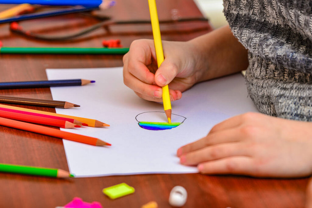 Ένα κορίτσι ζωγραφίζει μια καρδιά με χρωματιστά μολύβια σε ένα λευκό φύλλο ανάμεσα στα παιδικά παιχνίδια. - Φωτογραφία, εικόνα
