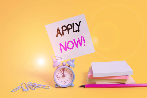 Conceptual hand writing showing Apply Now. Concept meaning request something officially in writing or by sending in form Alarm clock pencil clips note stacked notepads colored background - Photo, Image