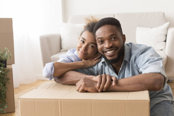 Афро-супруги обнимаются среди распакованных коробок в новой квартире
 - Фото, изображение