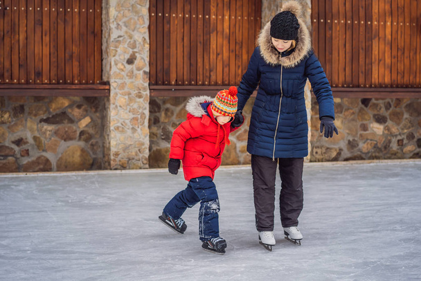 young mother teaching her little son ice skating at outdoor skating rink. Family enjoy winter on ice-rink outdoors - Foto, Bild