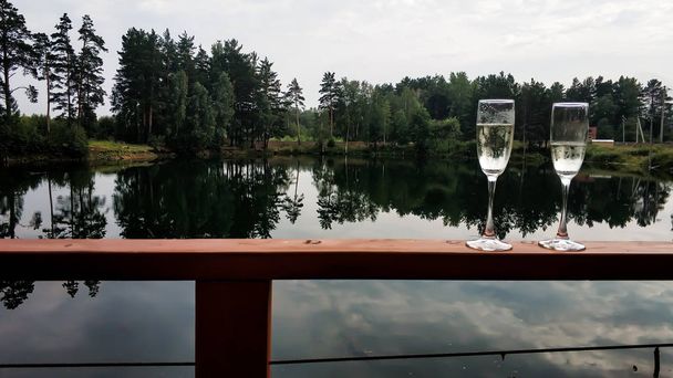 Deux verres avec du vin mousseux sur la rampe sur le fond du lac - Photo, image