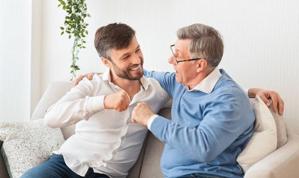 Son And Father Bumping Fists Sitting On Couch At Home - Photo, Image
