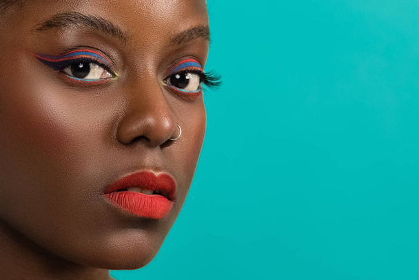 Allegro giovane donna africana con trucco vivido sui suoi occhi contro lo sfondo blu
. - Foto, immagini