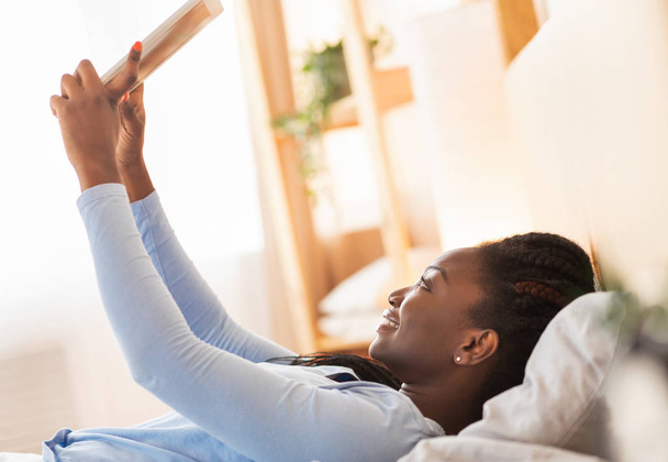 Afro κορίτσι χρησιμοποιώντας tablet ξαπλωμένη στο κρεβάτι το πρωί - Φωτογραφία, εικόνα
