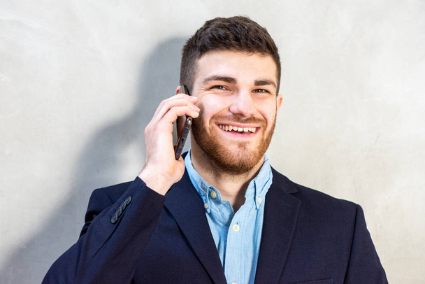 Close up portrait of young businessman with beard talking with cellphone - Foto, Imagen