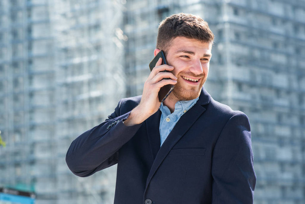 Şehirde cep telefonuyla konuşan mutlu genç iş adamının portresini kapat. - Fotoğraf, Görsel