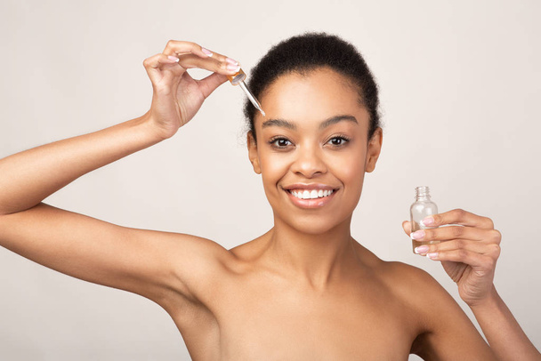 Ragazza afroamericana che applica olio cosmetico sul viso, sfondo beige
 - Foto, immagini