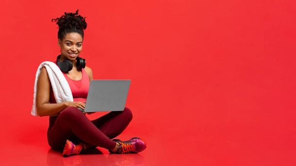 Smiling sporty athletic woman using laptop over red background - Valokuva, kuva