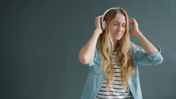 Joyful girl dancing enjoying music in headphones against black backgrond - Video