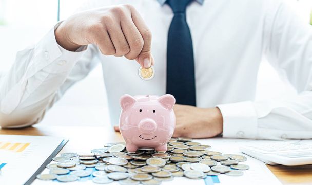 Hand holding a pink piggy bank coin, Businessmen prepare a financial plan by accounting income - expenses for stable business growth saving ideas, Saving money concept - 写真・画像