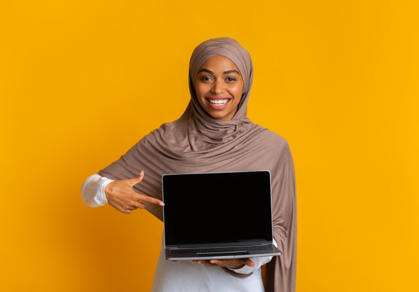 Афро-мусульманка Дівчина в головному шарфі тримає лаптоп комп'ютер з чорним екраном - Фото, зображення