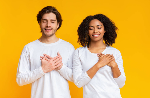 Grato casal interracial mantendo as mãos no peito, expressando gratidão
 - Foto, Imagem