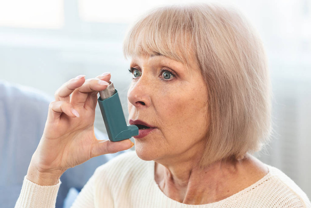 Elderly woman using asthma inhaler for allergies - Foto, afbeelding