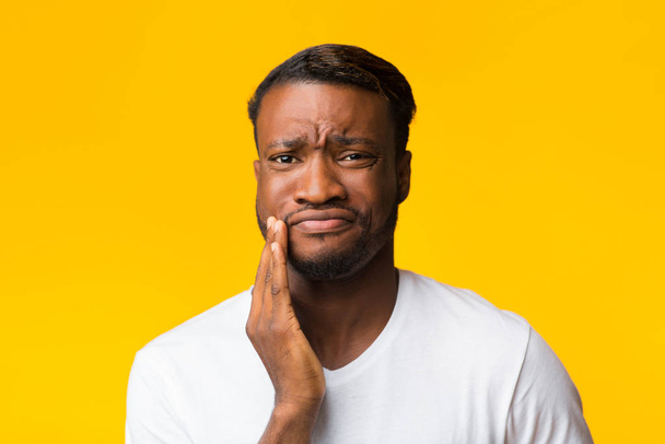 trauriger afrikanisch-amerikanischer Mann mit schmerzenden Zähnen vor gelbem Hintergrund - Foto, Bild