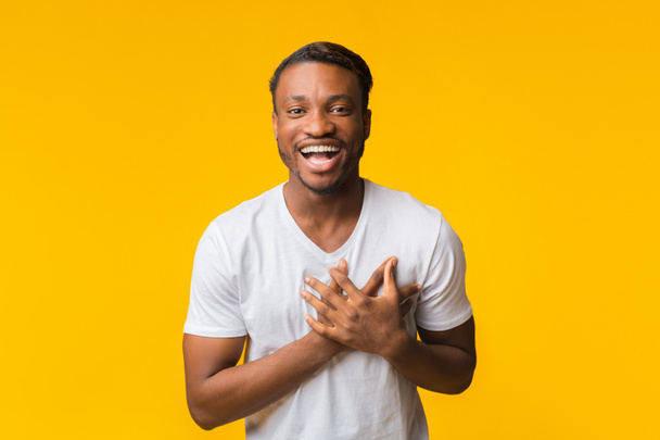 Hombre afroamericano riendo tocando el pecho parado sobre fondo amarillo
 - Foto, imagen