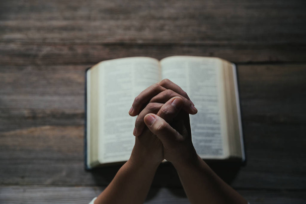 Mãos dobradas em oração em uma Bíblia Sagrada no conceito da igreja para a fé
 - Foto, Imagem