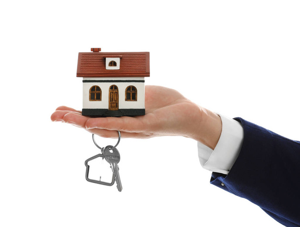 Real estate agent holding house model and key on white background, closeup - Foto, Bild