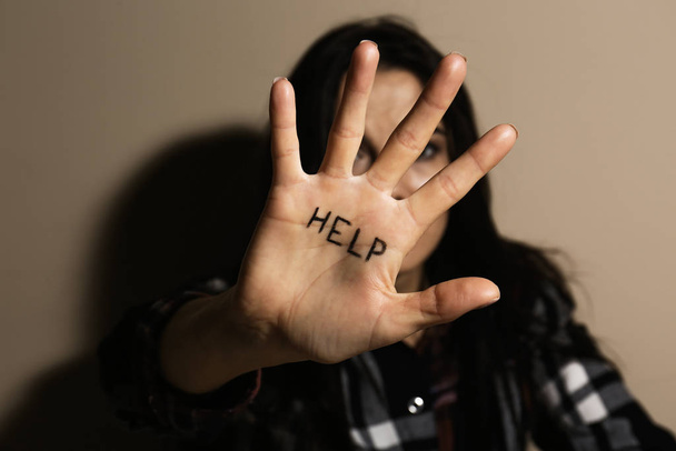 Abused young woman showing palm with word HELP near beige wall, focus on hand. Domestic violence concept - Фото, зображення