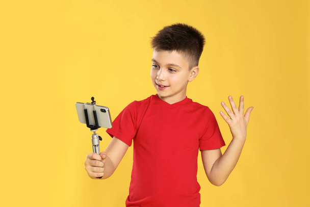 Cute little blogger recording video on yellow background - Foto, Imagem