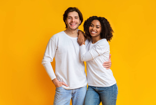 Retrato de casal mestiço sorridente posando sobre fundo amarelo em estúdio
 - Foto, Imagem