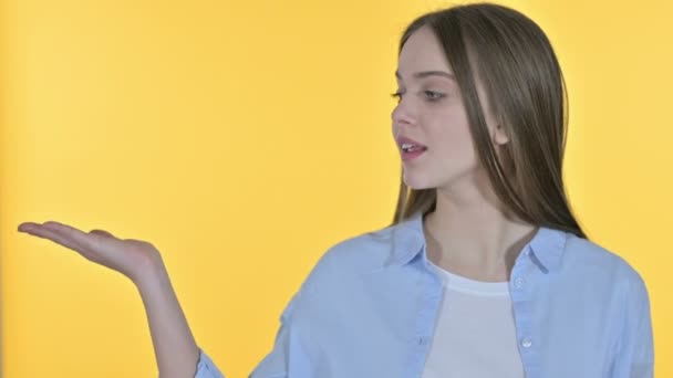 Jovem mulher mostrando produto na mão, fundo amarelo
 - Filmagem, Vídeo