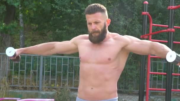 Bodybuilder demonstrates muscles. Young bearded athletic bodybuilder plays sports outdoors - Footage, Video