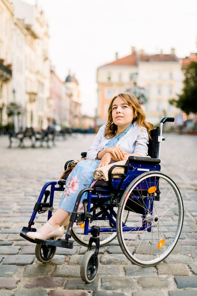 Gelukkige jonge vrouw in rolstoel buiten, poseren op de achtergrond van oude gebouwen in de stad - Foto, afbeelding