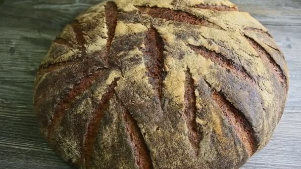 zoom z velké celé domácí kulaté černý žitný chléb se zajímavou texturou povrchu na tmavém dřevěném stole - Záběry, video