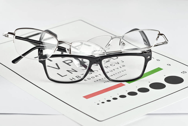 Glasses on a white background. Background with letters for vision test. Many glasses are dropped. - Foto, immagini