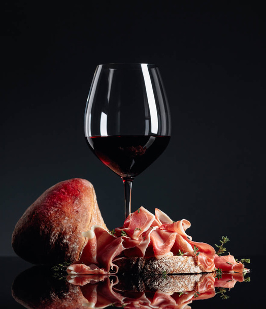 Prosciutto with ciabatta, red wine and thyme on a black backgrou - Foto, Bild