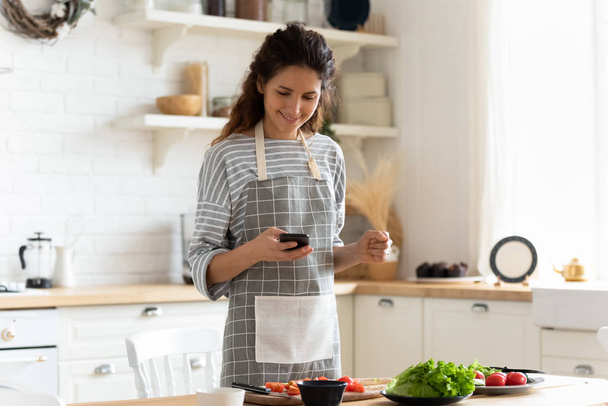 Mujer sosteniendo teléfono inteligente utilizando aplicaciones de cocina sitios web buscar recetas
 - Foto, Imagen