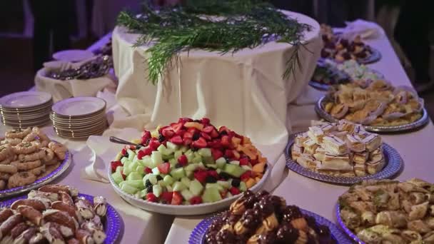 panorama dole na bohatě zdobeném svatebním banketovém stole servírované s nejrůznějšími sušenkami a krájeným ovocem na velkých kovových podnosech - Záběry, video
