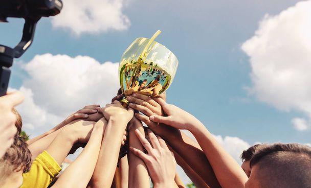 Kids in sports team lift up the golden cup trophy after winning the final tournament match. Children celebrate success in sports. Winning championship in sport - Photo, Image
