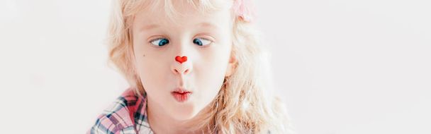 Cross-eyed kid looking at red heart sticker on her nose. Funny h - Photo, Image