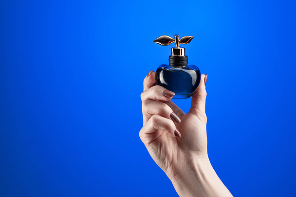 perfume in female hands on a blue background - Φωτογραφία, εικόνα
