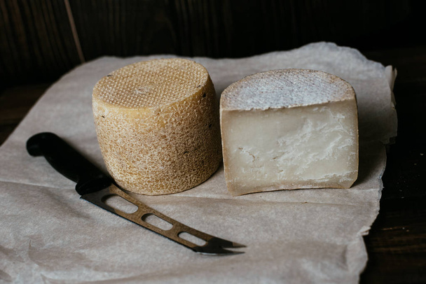 Kravot de queijo duro ou parmesão em um conselho escuro de madeira. Faca de queijo ao lado das cabeças de queijo
 - Foto, Imagem