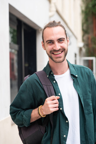 Portrét mladého muže s batohem usmívajícím se ve městě - Fotografie, Obrázek