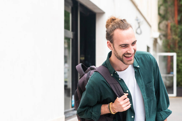 Portrait of young man with backpack laughing in city - Photo, image