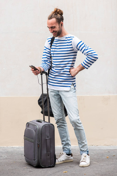 Portret podróżnika z walizką i telefonem komórkowym przy białej ścianie - Zdjęcie, obraz