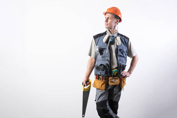 Builder with a saw. In work clothes and a helmet. On a light gray background. - Photo, Image