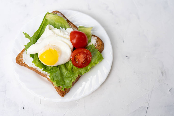 Sandwich with fried eggs salad and tomato on a white plate on a white background. - Foto, Bild