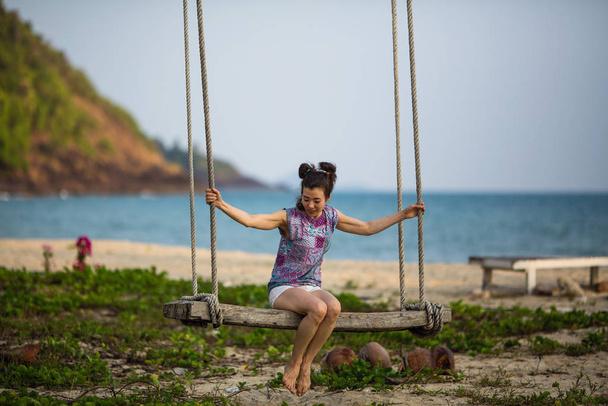 Mujer asiática balanceándose en un columpio en una playa tropical
. - Foto, Imagen