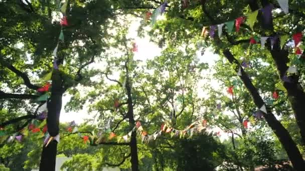 Guirnalda festiva de banderas de papel multicolores para las vacaciones. Paisaje para una fiesta de cumpleaños de niños. Decoración sobre la naturaleza contra el telón de fondo de los árboles. Bunting banner - banderas de colores de hojas
. - Metraje, vídeo